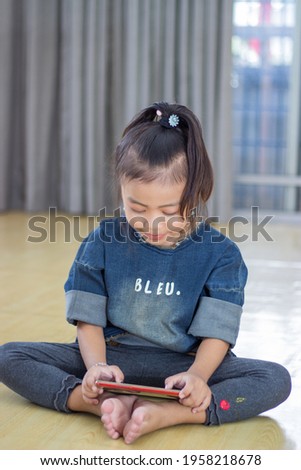 Cute preschooler little girl wearing in jeans clothes, sitting, using modern smartphone, smart small kid browsing surfing internet watch cartoon on cellphone, easy access, blank copy space