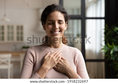 Thank you my God. Happy peaceful millennial hispanic lady stand alone with closed eyes keep hands close to heart hope pray in mind. Emotional young woman express deep gratitude impressed by good deed Royalty-Free Stock Photo #1958232697