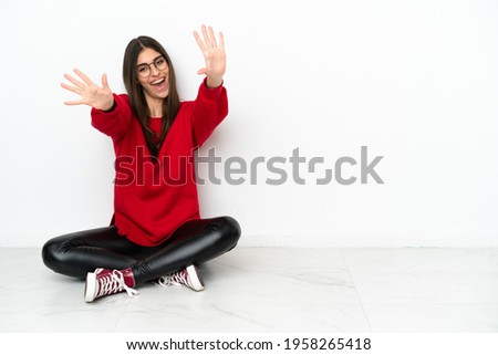 Young woman sitting on the floor isolated on white background counting ten with fingers