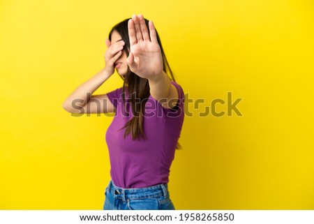 Young caucasian woman isolated on yellow background making stop gesture and covering face