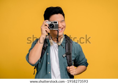 Portrait of a young backpacker Asian tourist taking a picture on a yellow background. He is very happy.