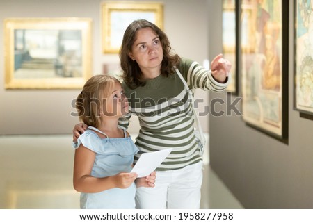 Young woman with daughter looking at painting in the museum of arts