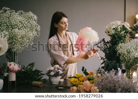 Young woman florist working in her flower studio, making beautiful bouquet using fresh plants and flowers. Small business. 