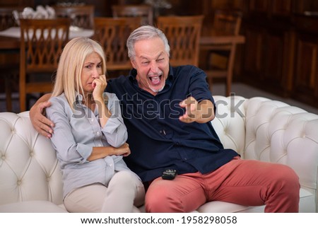 Man having a good laughter, his wife cries while watching the same tv program, lack of empathy concept Royalty-Free Stock Photo #1958298058