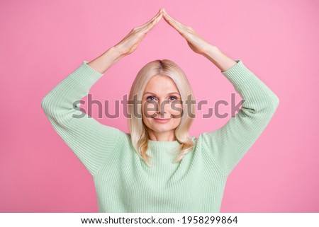 Photo portrait of old woman making roof over head with hands isolated on pastel pink colored background