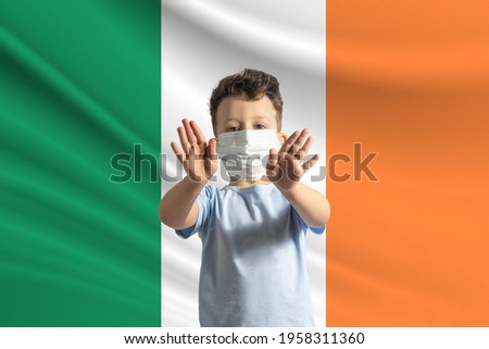 Little white boy in a protective mask on the background of the flag of Ireland Makes a stop sign with his hands, stay at home Ireland.