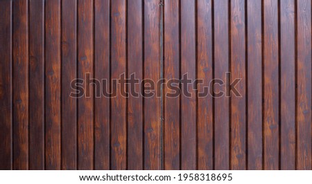part of a fence or wall made of narrow metal panels stylized as dark stained wood, a fragment of gate leaves made of textured fake wood and with a flat smooth surface