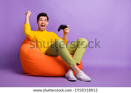 Full body profile side photo of young man happy rejoice victory video game joystick chair bean isolated over violet color background