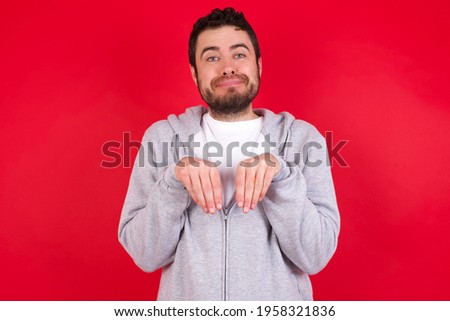 young handsome caucasian man in sports clothes against red background makes bunny paws and looks with innocent expression plays with her little kid