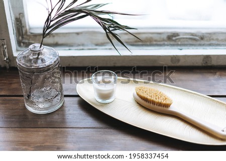 Details of interior, aromatic candle in glass and wooden brush with natural bristles on the metal tray on wooden window sill