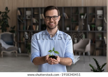 Portrait of smiling young businessman hold soil and small plant launch startup project or activity. Happy millennial male employee or CEO with seedling sprout in hands. Growth, development concept.