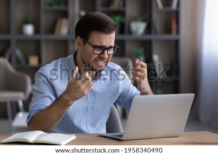 Unhappy millennial male employee work online on laptop at home office frustrated by gadget error or mistake. Angry young Caucasian man stressed with computer operational problem or breakdown. Royalty-Free Stock Photo #1958340490