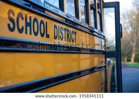 School District written on the side of a school bus. Door is open. No people, nature background.
