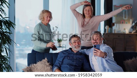 Caucasian old friendly men and women dancing watching music concert TV show on large monitor in the living room. Relationships. Old friends.