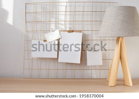 Poster, cards mock up attached on gold grid board with binder. Natural beige colors interior part with desk and table lamp, mood board template. Empty white various sizes paper on light wall