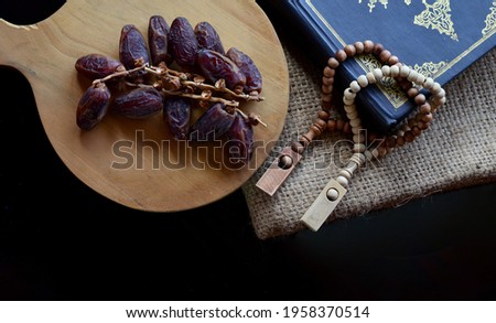 Holy Quran with beads and dates fruit againts dark background close up