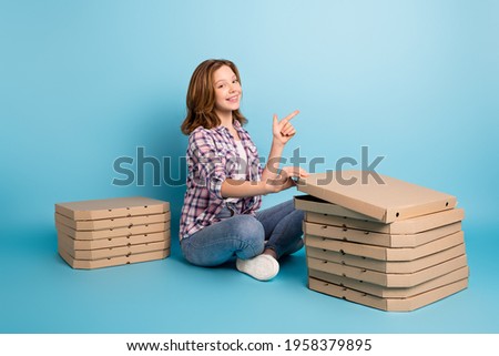Full size profile photo of optimistic red hairdo girl sit point empty space eat pizza from boxes wear shirt isolated on blue background