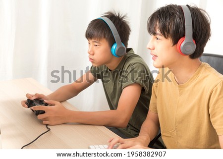 Two teenage boys with headphone using computers to play online gaming at home. Happy Asian kid enjoy online game at home.