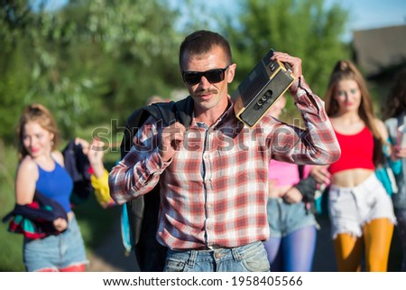 Funny man with a cassette recorder in front of a group of girls. People in the style of the nineties.