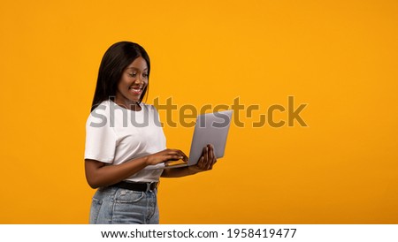 Happy african american young woman using newest laptop, surfing on Internet or checking social media, yellow studio background, panorama with copy space. Modern technologies concept