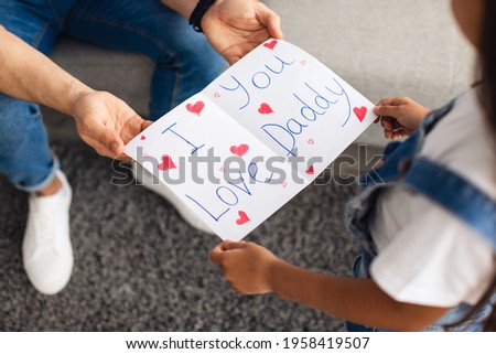 Above top high abgle view of little girl greeting her father, holding and giving poster card with I Love You Daddy text, young man receiving congratulations from daughter