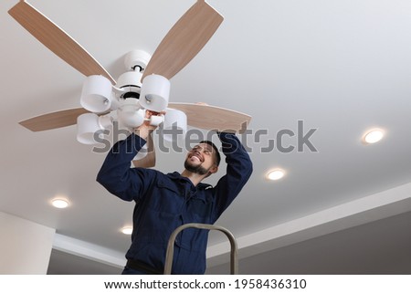 Electrician repairing ceiling fan with lamps indoors Royalty-Free Stock Photo #1958436310