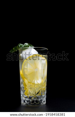 
Glass of refreshing lemonade, fruit cocktail with lemon slices, mint branch and ice on black background