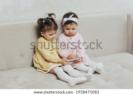 Cute children sitting at home on couch and is using internet app on mobile phone watching online cartoons. 