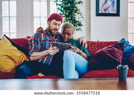 Diverse hipster guys hug and reading received email message using home internet connection on modern touch pad, Caucaisan husband and African American wife in eyewear browsing wireless website