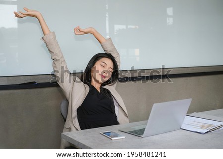 Young lady busiiness woman stretching her body on desk with smile and close eye, relaxing feeling after finished work action.