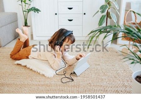 Girl with headphones using digital tablet device lying on floor in living room at home