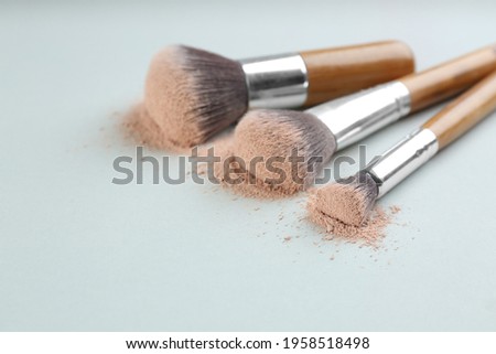 Different makeup brushes with crushed cosmetic product on light background, closeup. Space for text