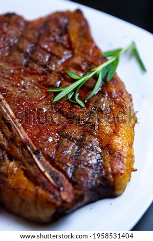 Delicious t-bone beef steak cooked on grill and served on white plate with rosemary herb in restaurant.Download royalty free curated images collection with gourmet foods for design template