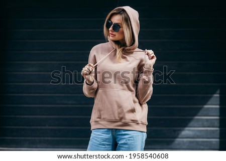 Fasion blonde woman in brown oversize hoodie, glasses and blue jeans, mockup for logo or branding design Royalty-Free Stock Photo #1958540608