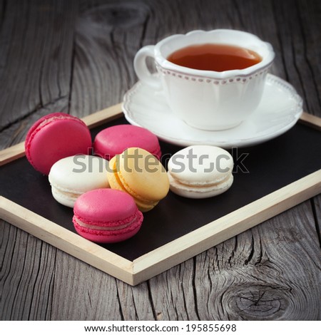 Colorful French macaroons and cup of tea on a dark rustic wooden background, selective focus
