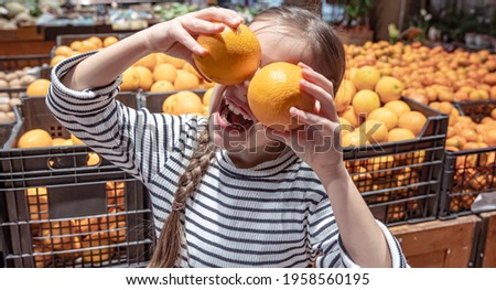 Cheerful little girl posing with oranges in a grocery store.