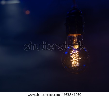 Close up of a glowing light bulb hanging in the dark copy space.
