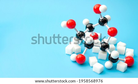 Simple sugars, diabetes awareness and chemical structure of carbohydrates concept with plastic model of the glucose molecule and sugar cubes isolated on blue background with copy space Royalty-Free Stock Photo #1958568976