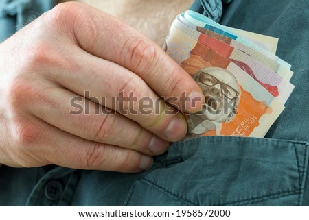 the man takes a bundle of columbian pesos from his shirt pocket  Royalty-Free Stock Photo #1958572000