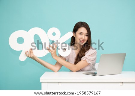 Portrait of Asian business woman showing and holding 90% number or ninety percent and sitting with laptop isolated over light green background