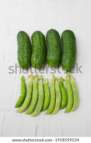 Pods of green peas lie with cucumbers on a light gray background.