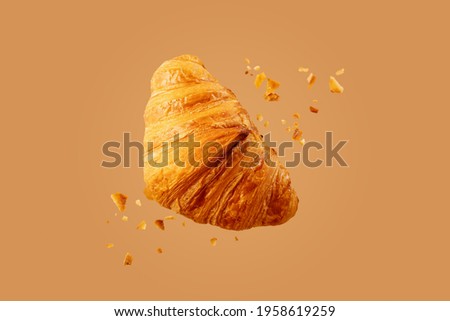 Freshly baked croissant flying in air. Close up of crumbled french croissant. Royalty-Free Stock Photo #1958619259