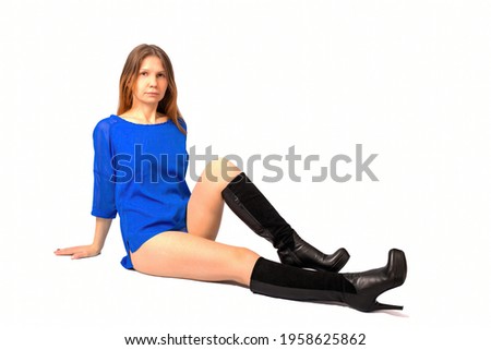 Portrait of a girl in a blue blouse and black boots on a light background. The girl is sitting. 