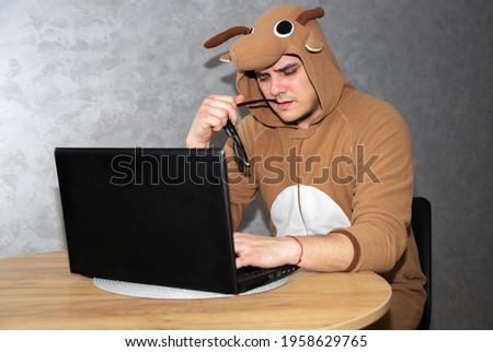 Office worker in cosplay costume of a cow. Guy in the funny animal pyjamas sleepwear near the laptop. Man is working from home. Search job, unemployment  concept, economy crisis. Remote work.