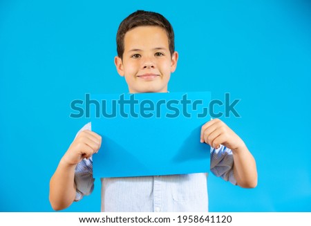 Cute boy showing a blue blank paper isolated over blue background