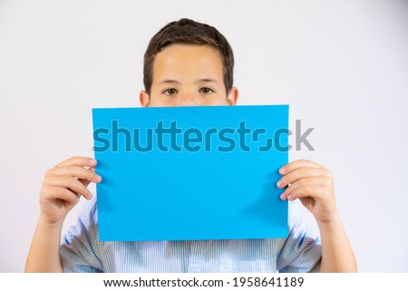 Closeup portrait of a boy holding blue blank paper covering mouth isolated over white background