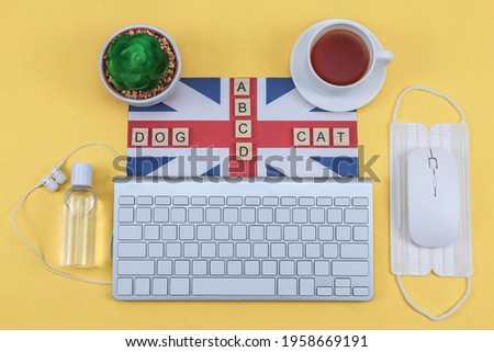 Keyboard, British flag, letters, words, disinfectant, tea and medical mask on a yellow background, top view close-up.
