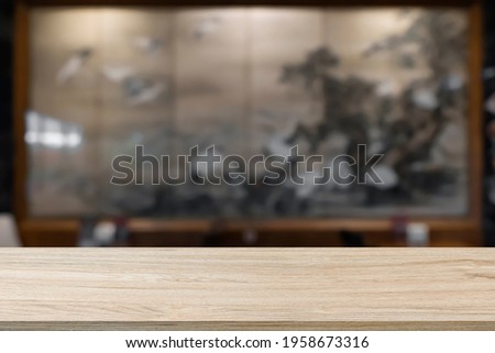 Empty wooden table with blur background of cafe and restaurant. With a large picture of art on the wall.