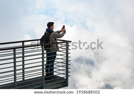Man standing on the observation desk and taking photos of clouds and mountains.