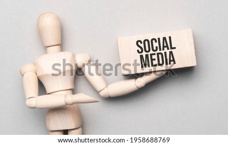 Wooden man shows with a hand to white board with text social media,concept